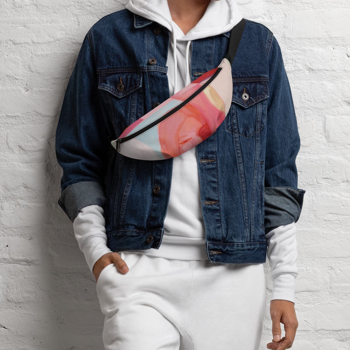 Person in a denim jacket and white hoodie wearing the "Being Human" belt bag with a pink and coral art print across the chest.