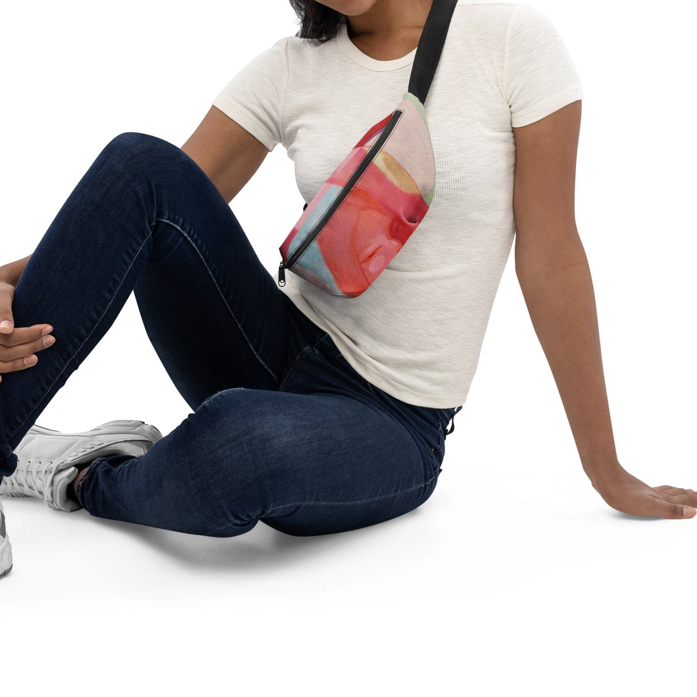 Seated person in a white T-shirt and jeans wearing the "Being Human" belt bag with an art print across the chest.⠋