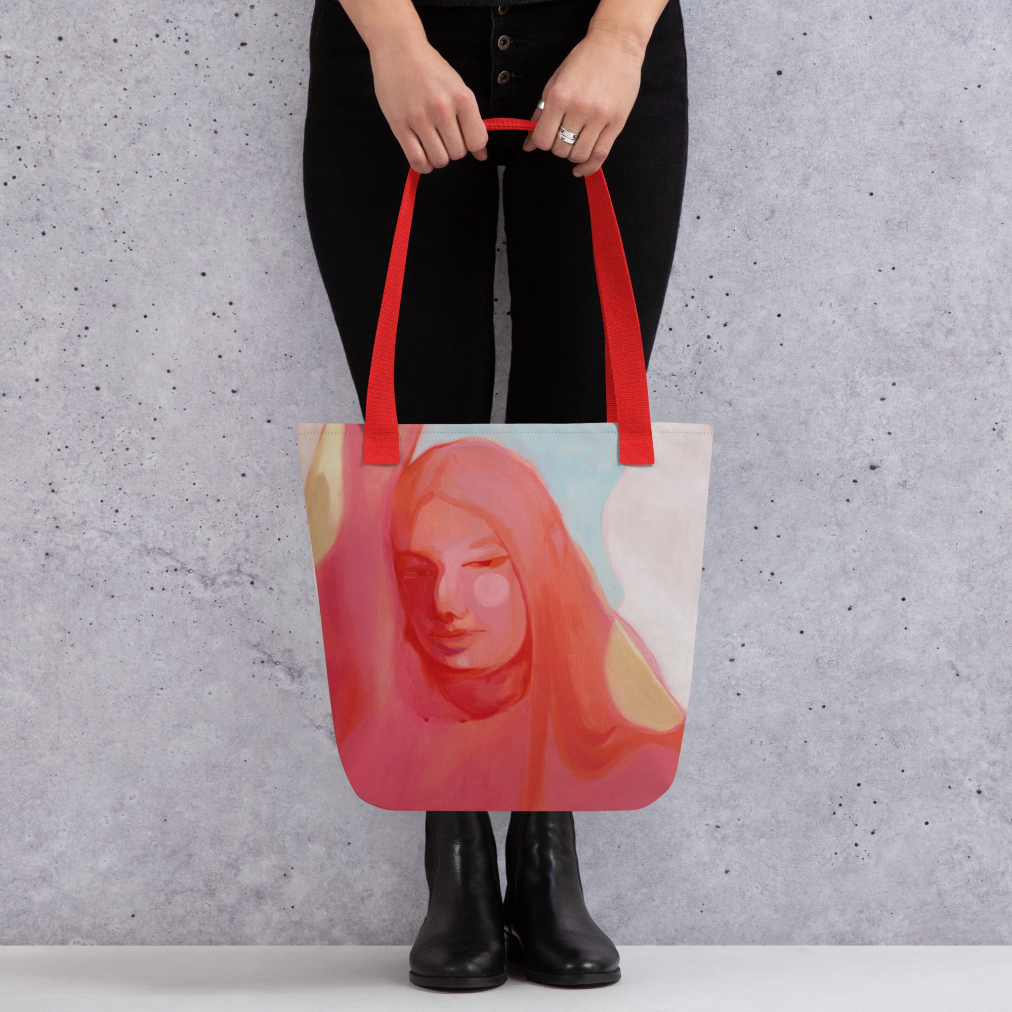 Person in schwarzer Kleidung hält die Stofftasche "Mensch Sein" mit roten Griffen, Rückseite mit spiegelverkehrtem Frauenporträt in Rosa- und Koralltönen.