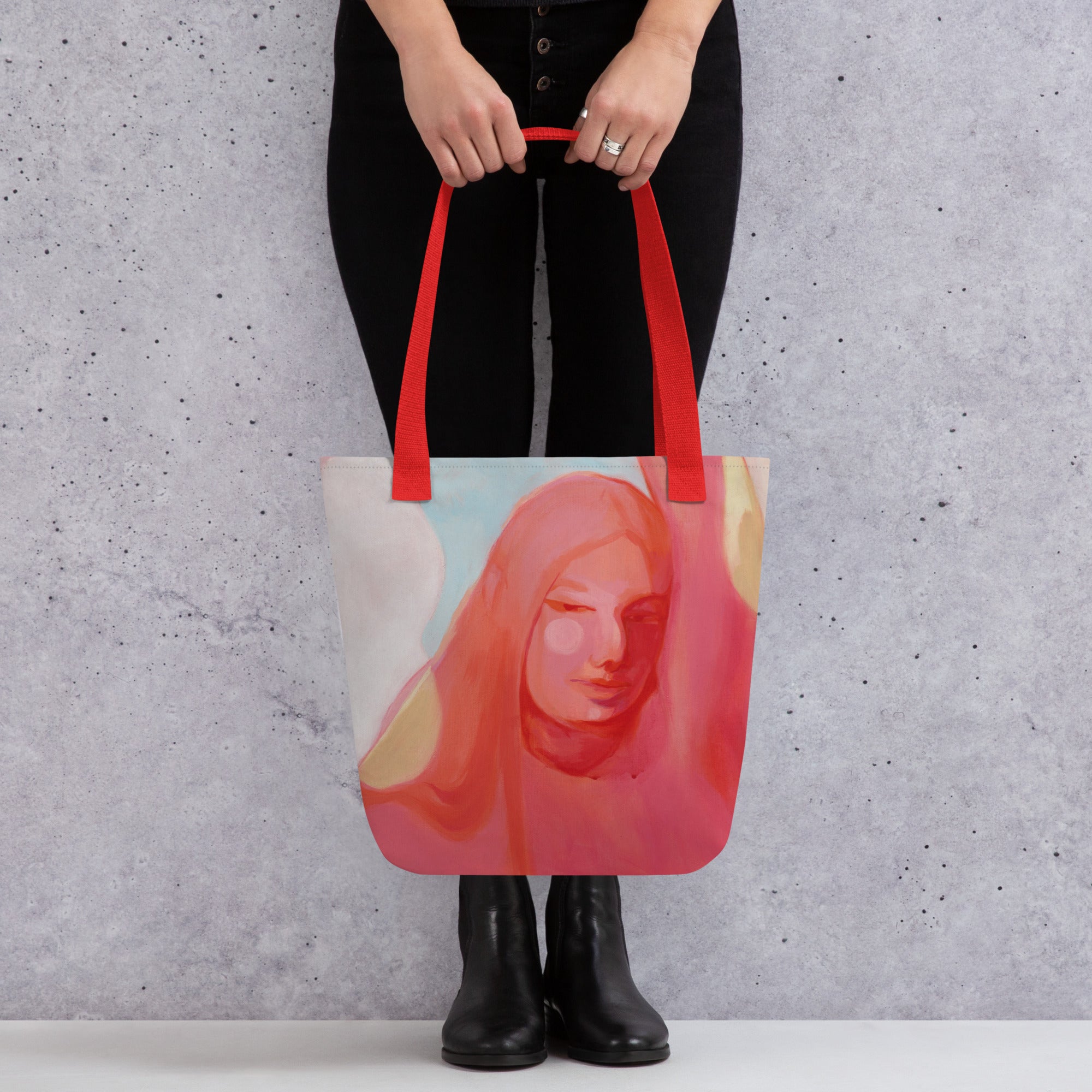  Person in schwarzer Kleidung hält die Tote Bag "Mensch Sein" mit roten Griffen vor den Beinen, das Frauenporträt ist frontal sichtbar.