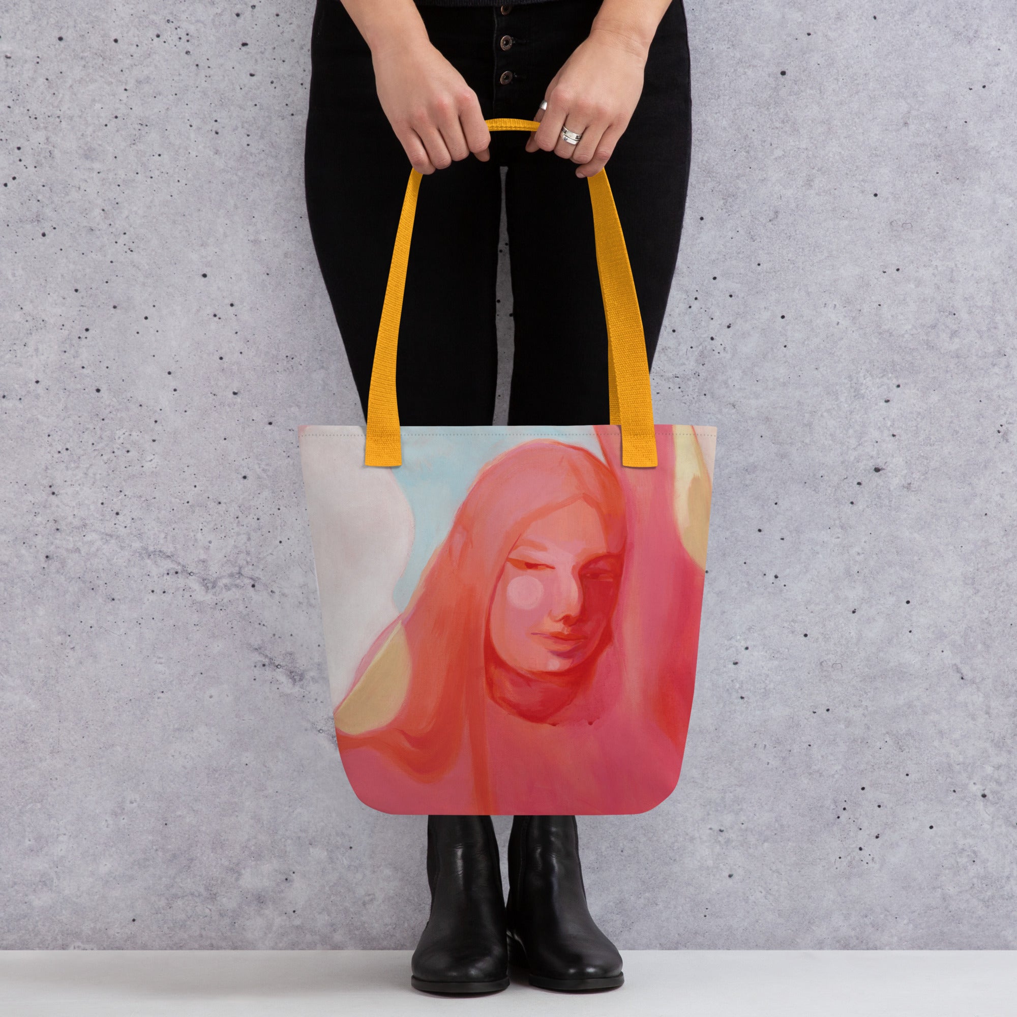 Person in schwarzer Kleidung hält die Tote Bag "Mensch Sein" mit gelben Griffen vor den Beinen, das Frauenporträt ist frontal sichtbar.
