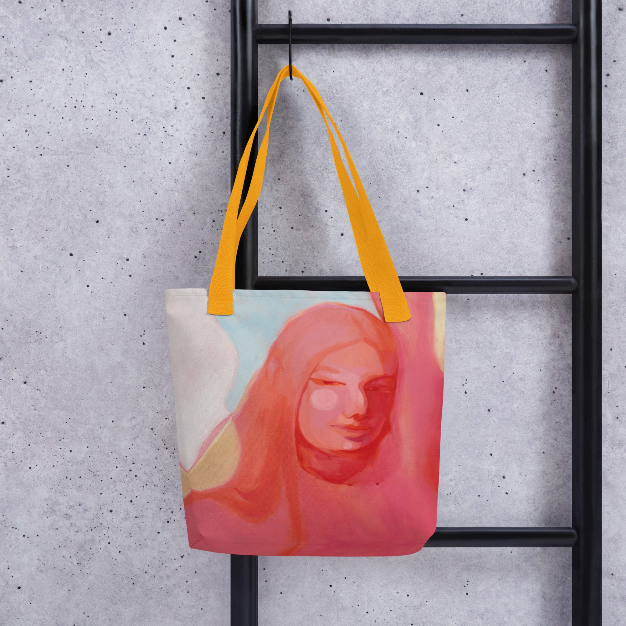 Tote Bag "Mensch Sein" mit gelben Griffen und Frauenporträt in Rosa- und Koralltönen, aufgehängt an einer schwarzen Metallleiter vor grauer Wand.